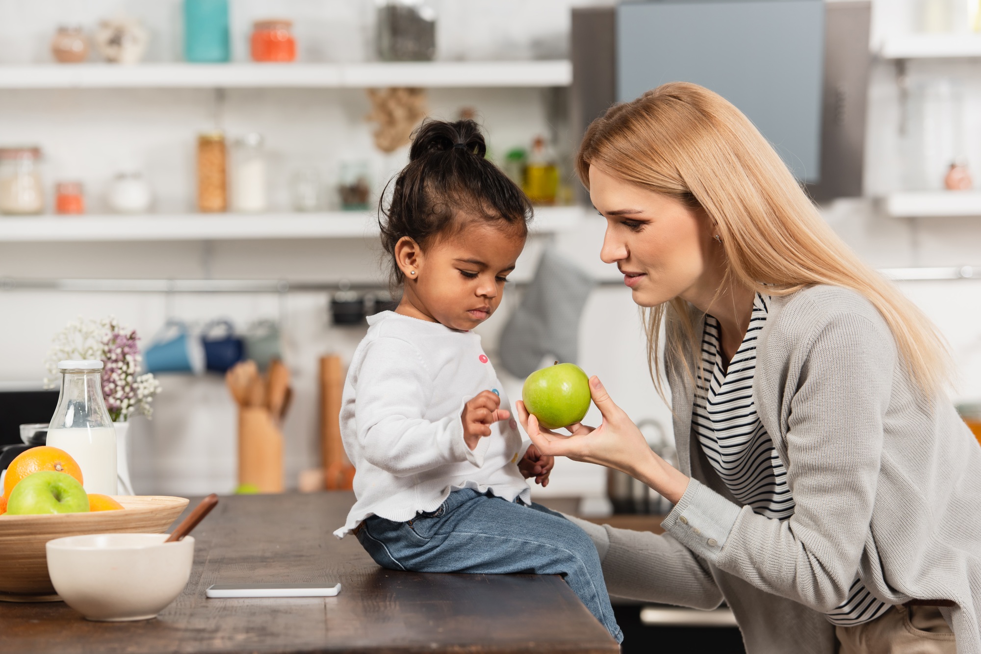 mother giving apple to adopted african american kid in kitchen