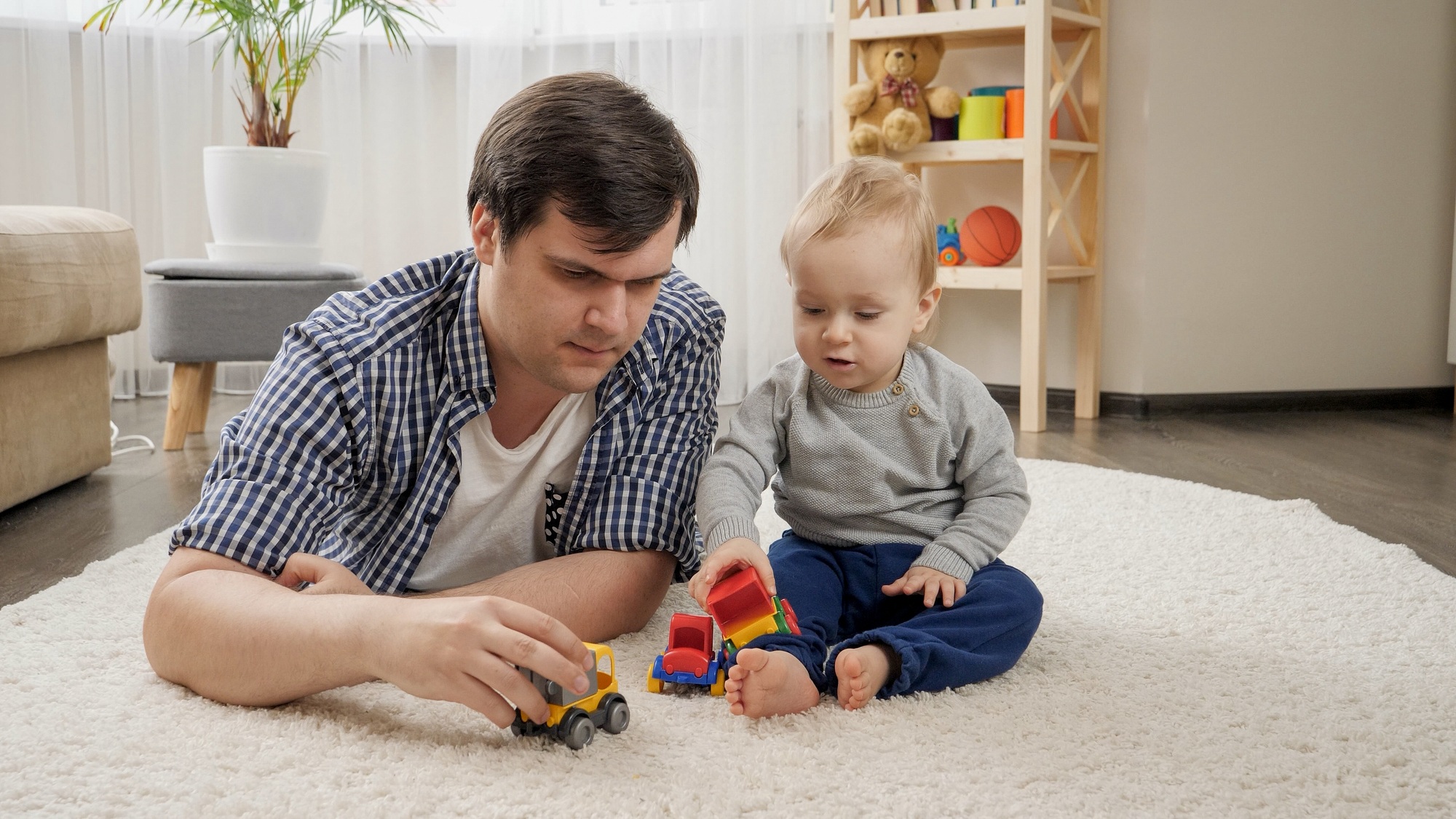 Young father lying with his baby son on carpet and playing toy cars.